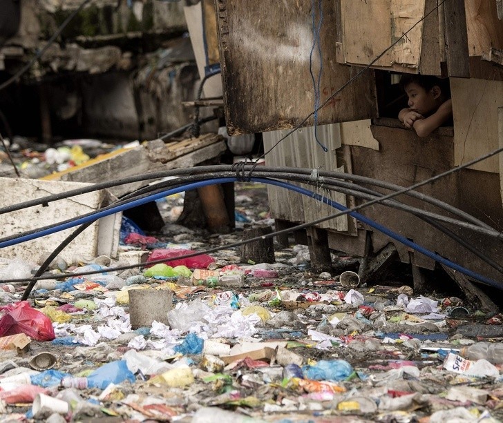 Chłopiec wyglądający przez okno przy wypełnionym śmieciami strumieniu w Manili.