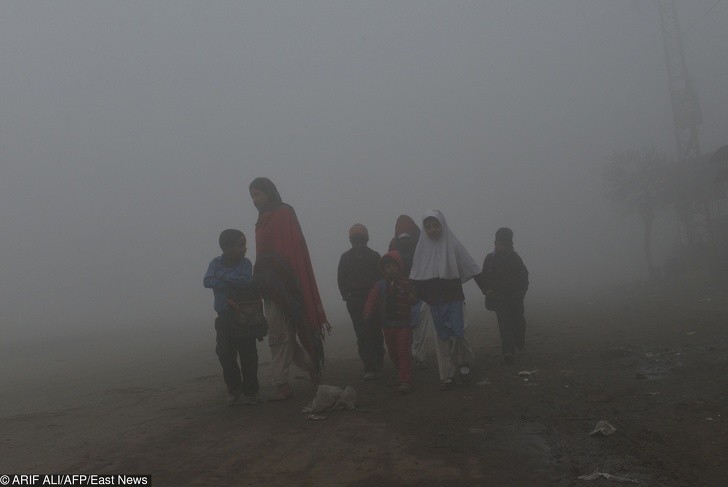 Pakistańska matka prowadząca swoje dzieci do szkoły w mgle i smogu.