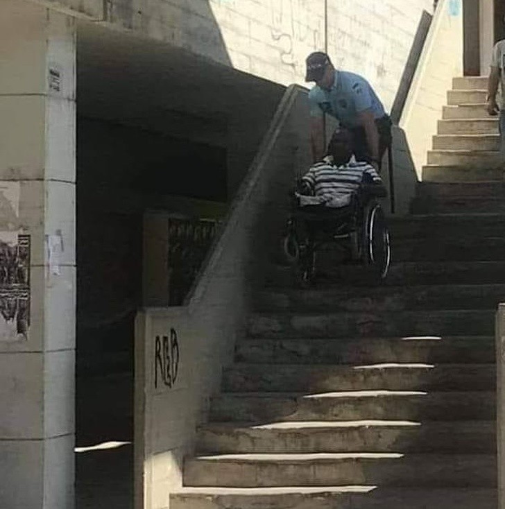Policjant pomagający niepełnosprawnemu mężczyźnie zjechać po schodach.