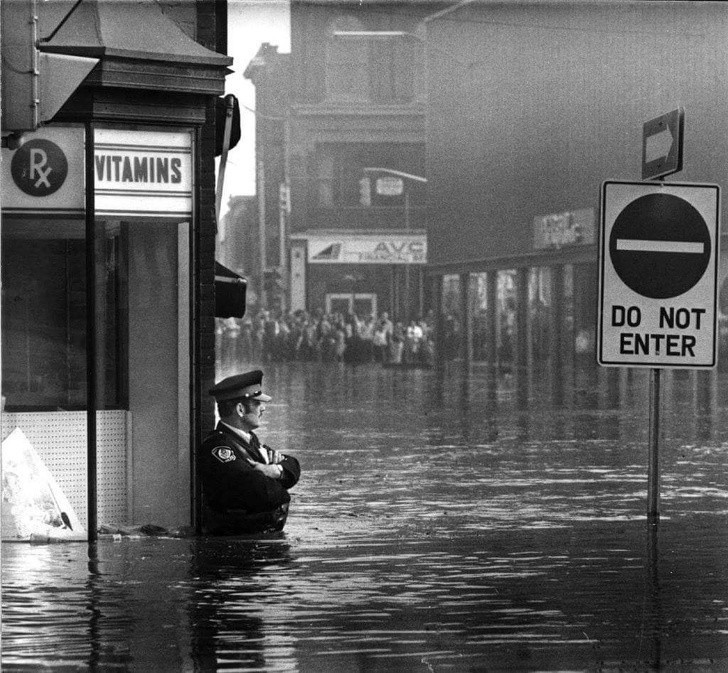 7. Oficer John Shuttleworth stojący po pas w wodzie podczas powodzi, Cambridge, Ontario, 1974