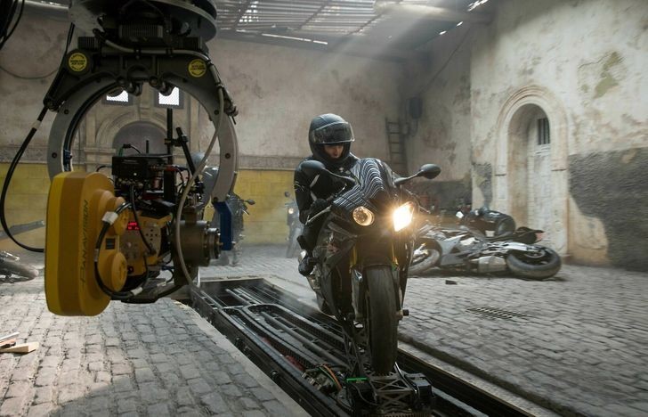 Rebecca Ferguson sėdi ant motociklo ant judančios platformos filmo „Mission: Impossible - Rogue Nation“ filmavimo aikštelėje