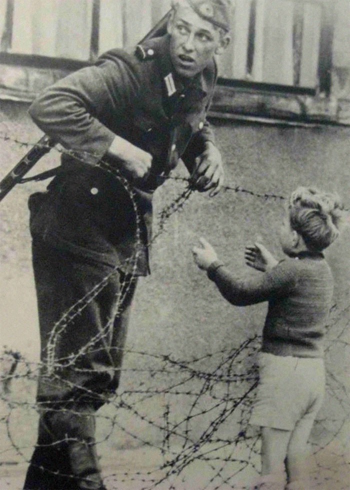 Niemiecki żołnierz pomaga małemu chłopcu przedostać się przez Mur Berliński, 1961