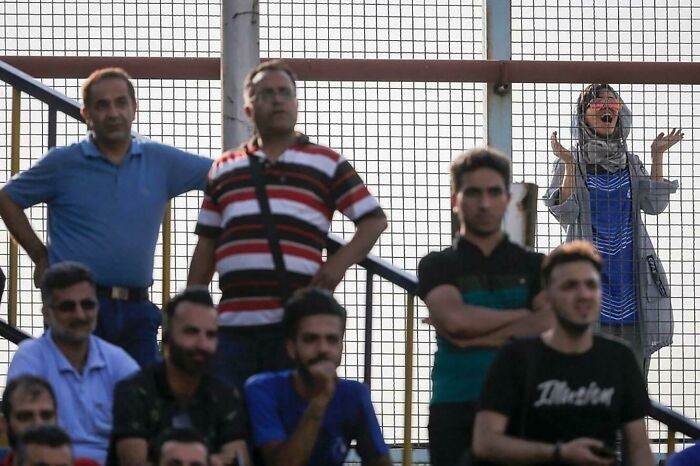 Irańska kobieta dopinguje swoją ulubioną drużynę piłkarską zza ogrodzenia, jako że w tym kraju kobietom nie wolno wchodzić na stadiony