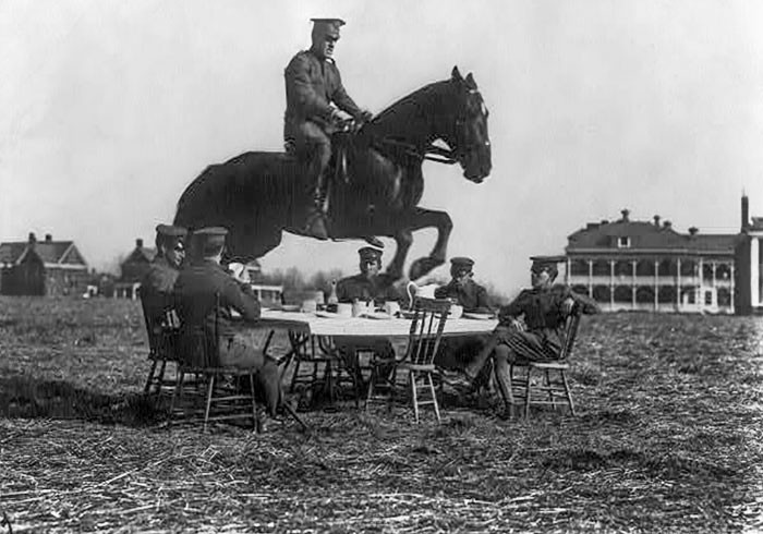 "Amerykańscy żołnierze siedzący przy stole, podczas gdy jeździec przeskakuje go na koniu"